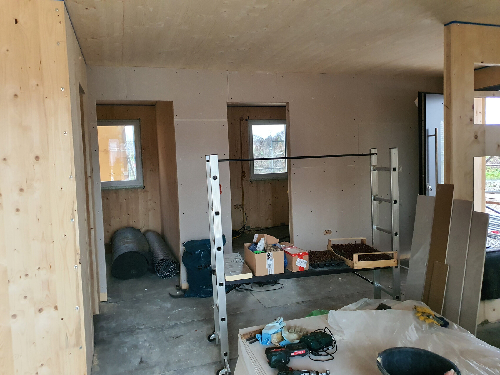 Unfertiger Innenraum eines Hauses: Trockenbauwände, Fenster, Bauwerkzeuge, Kartons und Metallregal.