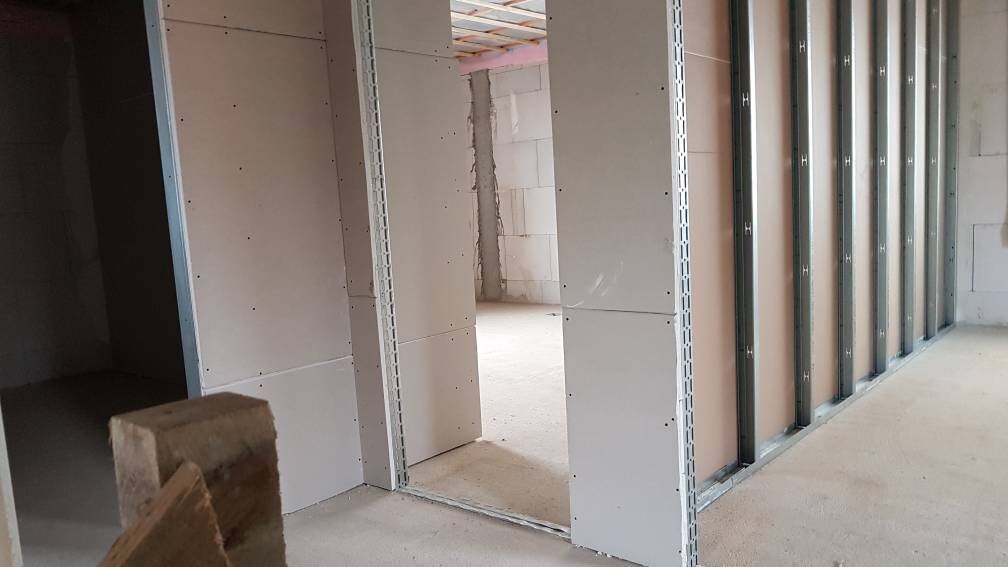 Innenraum einer Baustelle mit Metallständern, unfertigen Wänden und Türdurchgang.