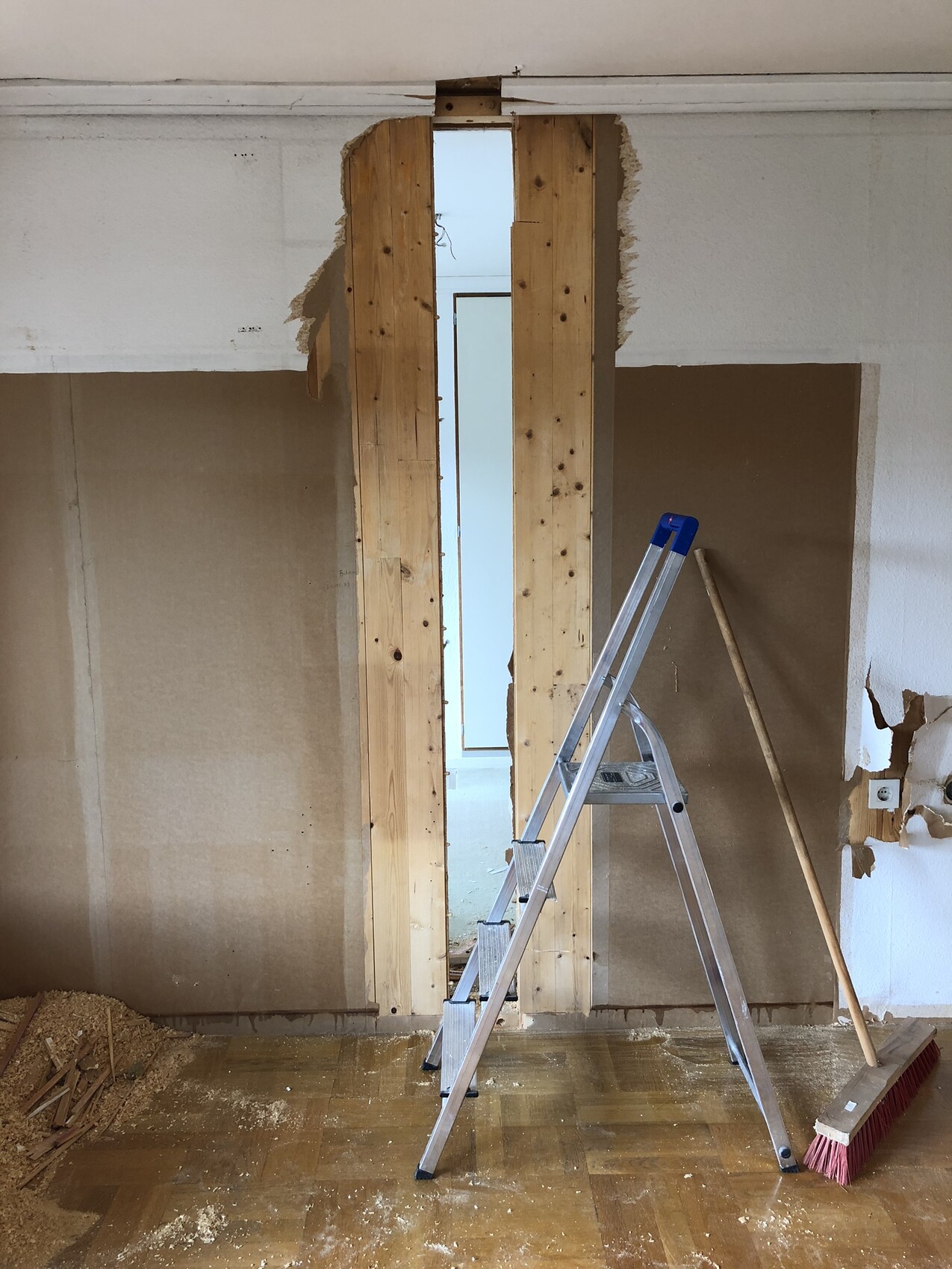 Renovierungsraum mit freigelegter Holzständerwand, Leiter, Besen und Baustaub auf dem Boden.