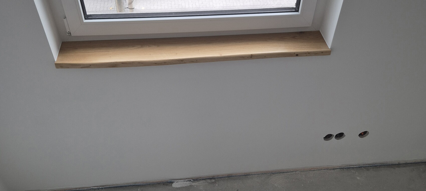 Unfertige Innenwand mit Holzfensterbank und drei runden Steckdosenlöchern am unteren Rand
