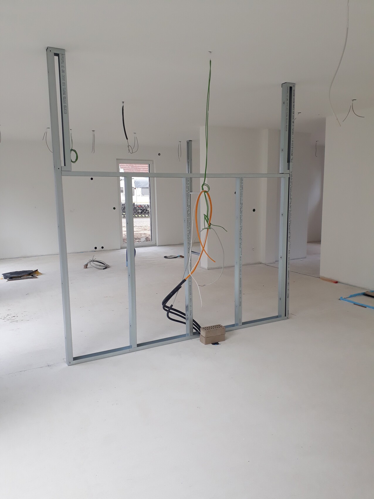 Halbfertige Innenwand mit Metallständern, lose Kabel hängen von der Decke; Bauwerkzeuge im Raum.
