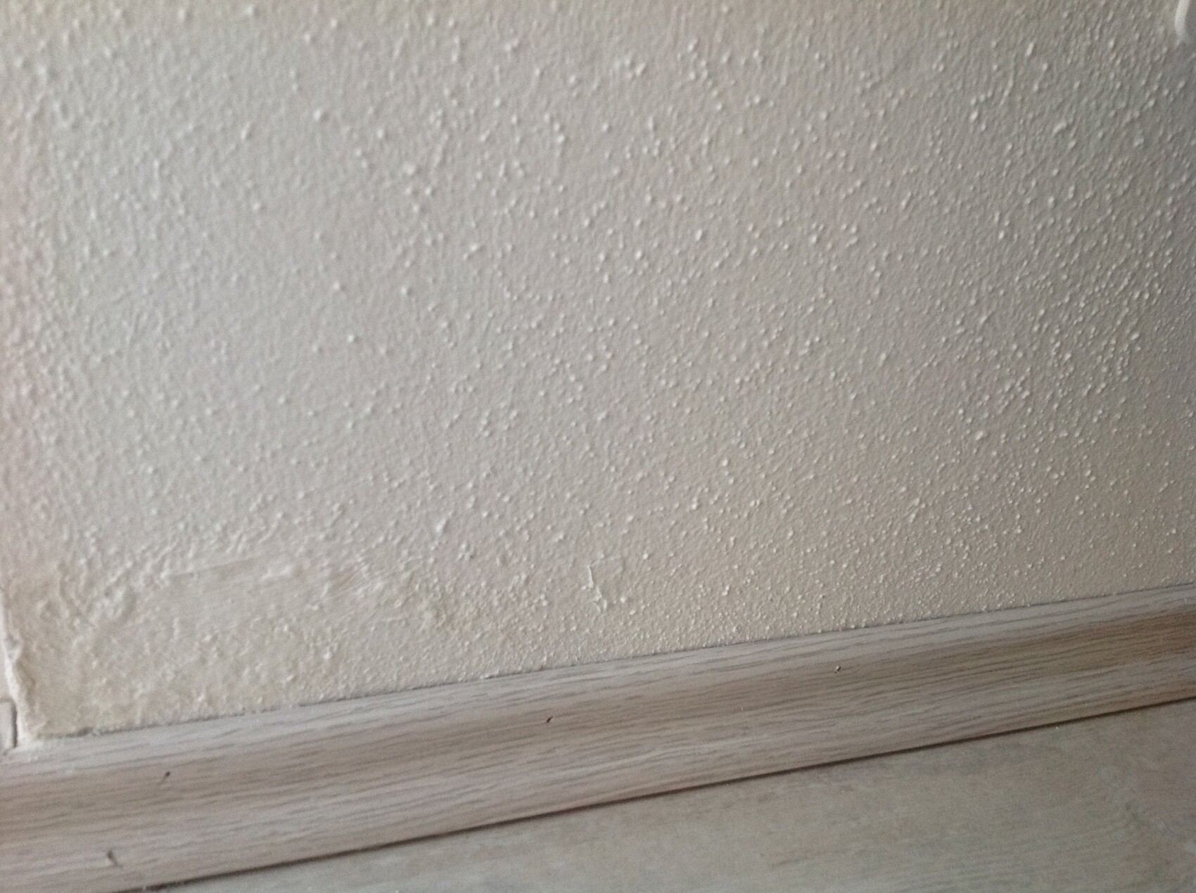 Weiße Innenwand mit strukturierter Oberfläche und einer Holzsockelleiste am Boden