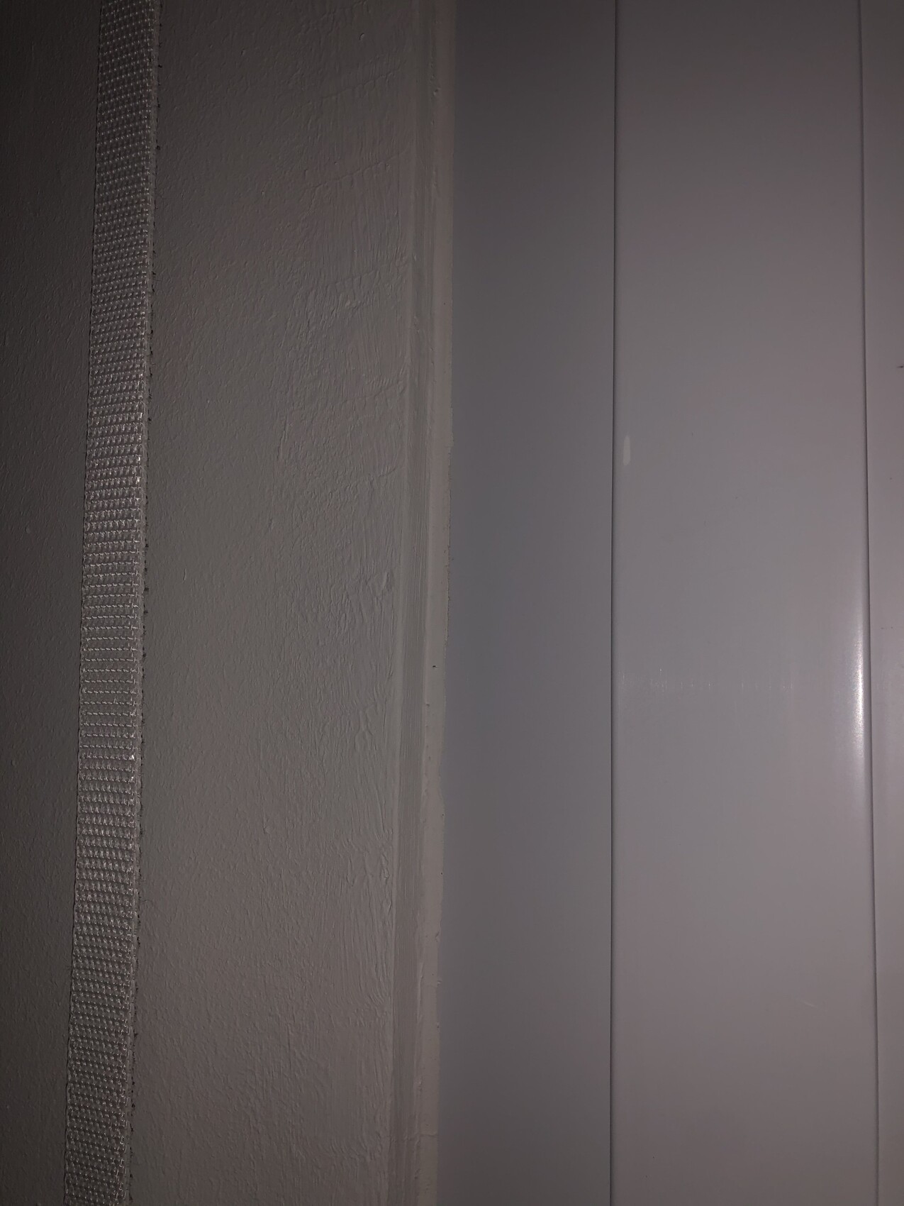 Nahaufnahme einer grauen Innenwand mit schmaler vertikaler Leiste und glatten Paneele.