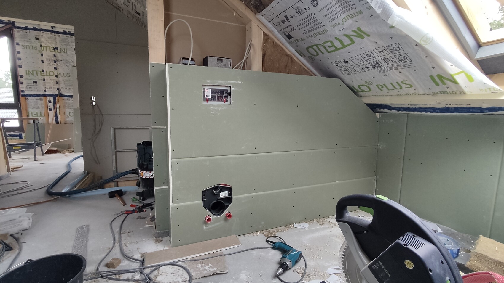 Große grüne Metallwand auf Baustelle mit Kabeln, Werkzeugen und Dämmmaterial.