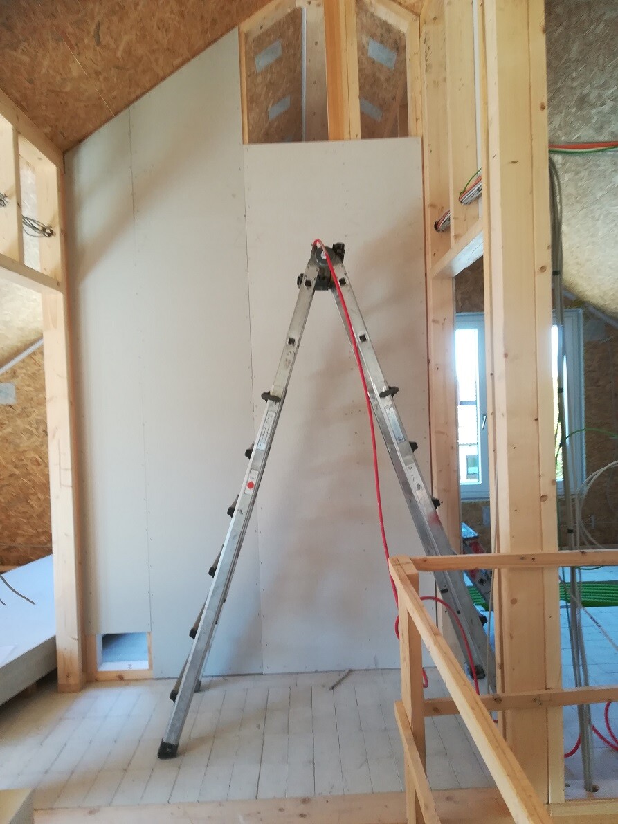 Aluminium-A-Leiter im Rohbau vor Trockenbauwand; rotes Kabel liegt über der Leiter.