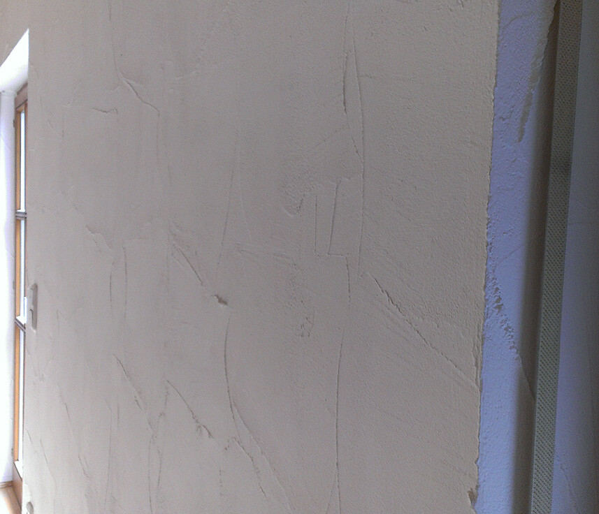 Innenwand mit rauem Verputz und Rissen, Fenster links sichtbar, Bauarbeiten im Innenraum