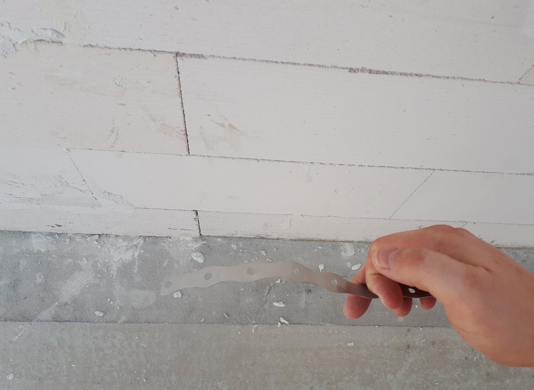 Hand hält Spachtel beim Verputzen einer hellen Wand auf einer Baustelle
