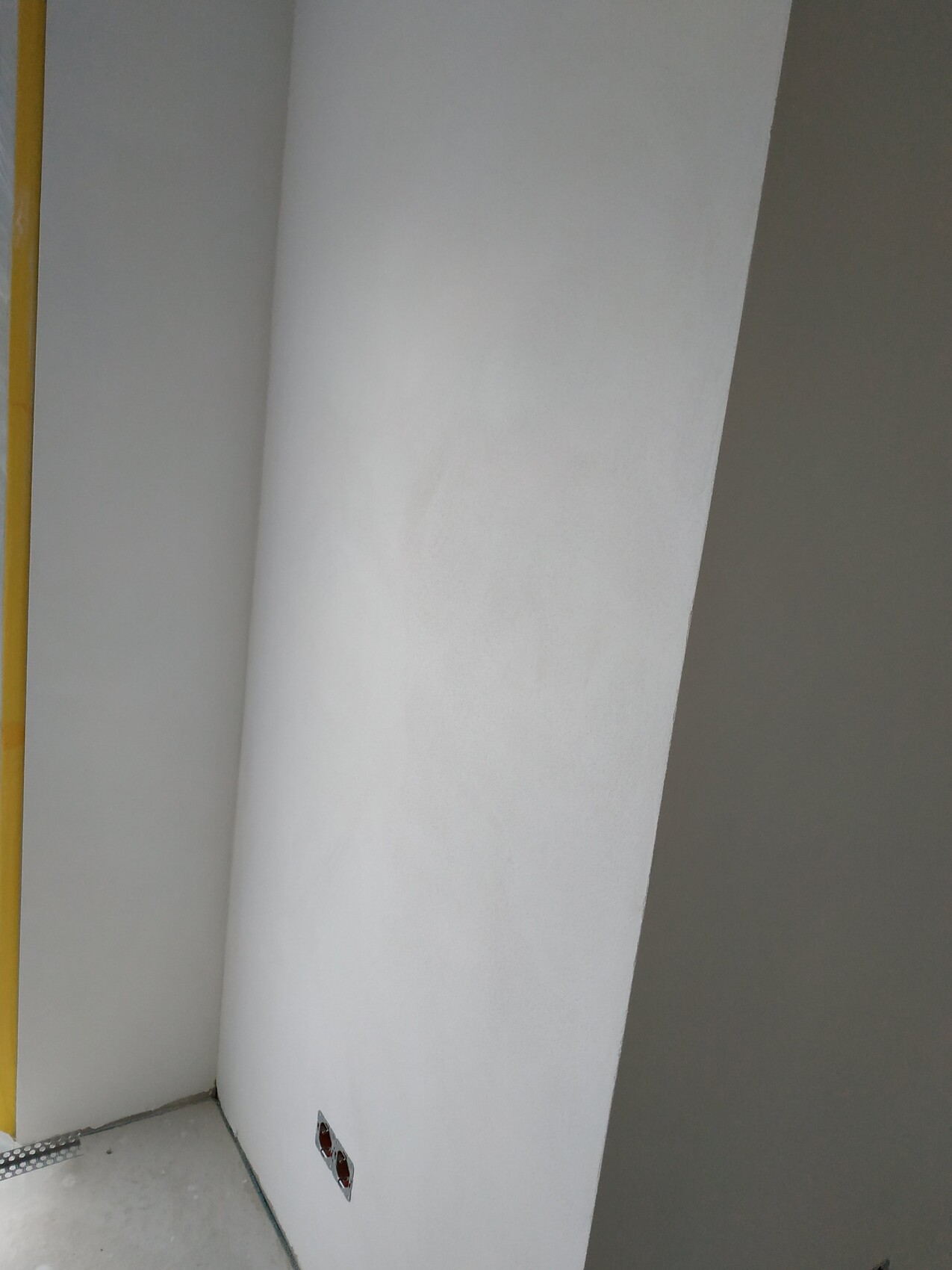 Weiße Innenwand mit runder Säule in der Ecke; Baubereich mit offenem Kabelauslass am Boden.