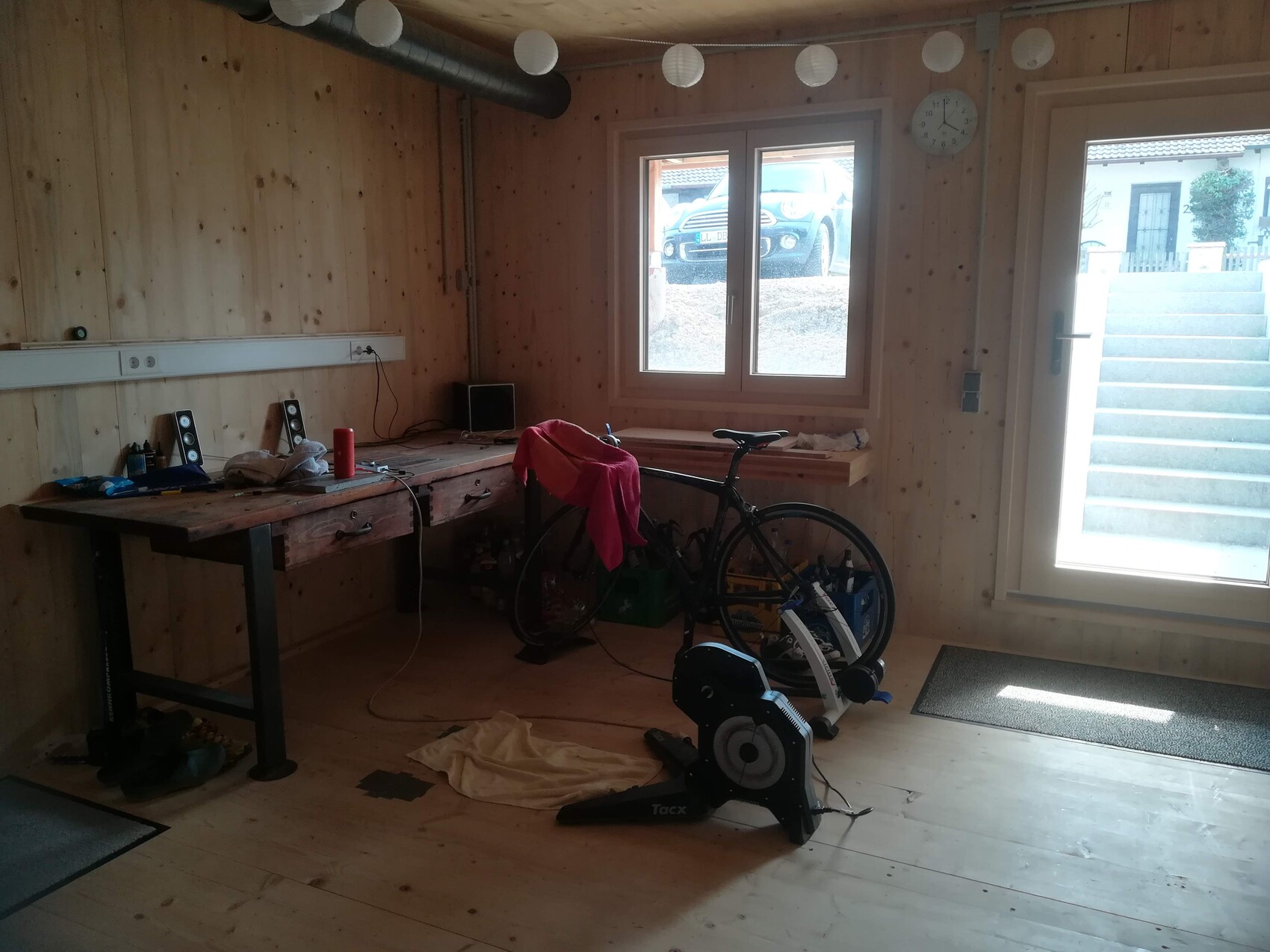 Heller Holzraum als Werkstatt mit Heimtrainer-Fahrrad, Werkbank, Werkzeug, großes Fenster und Tür.