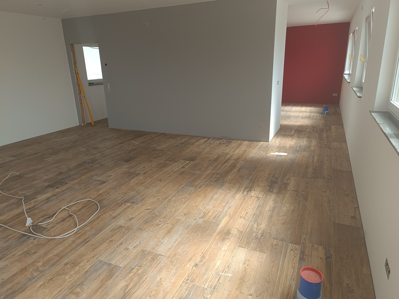Renovierter Innenraum mit Holzboden, grauen Wänden und roter Akzentwand am hinteren Ende.