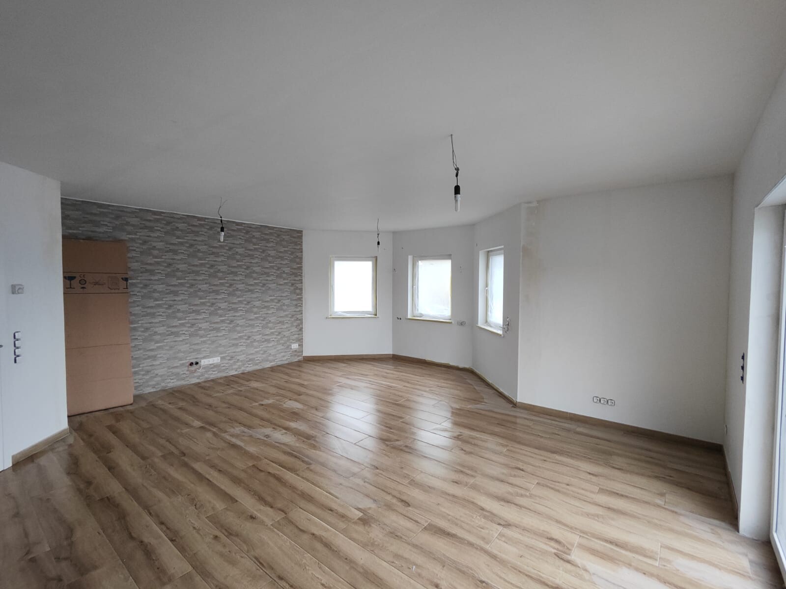 Heller Wohnraum zur Renovierung: Holzboden, Steinwand-Akzent, drei Fenster.