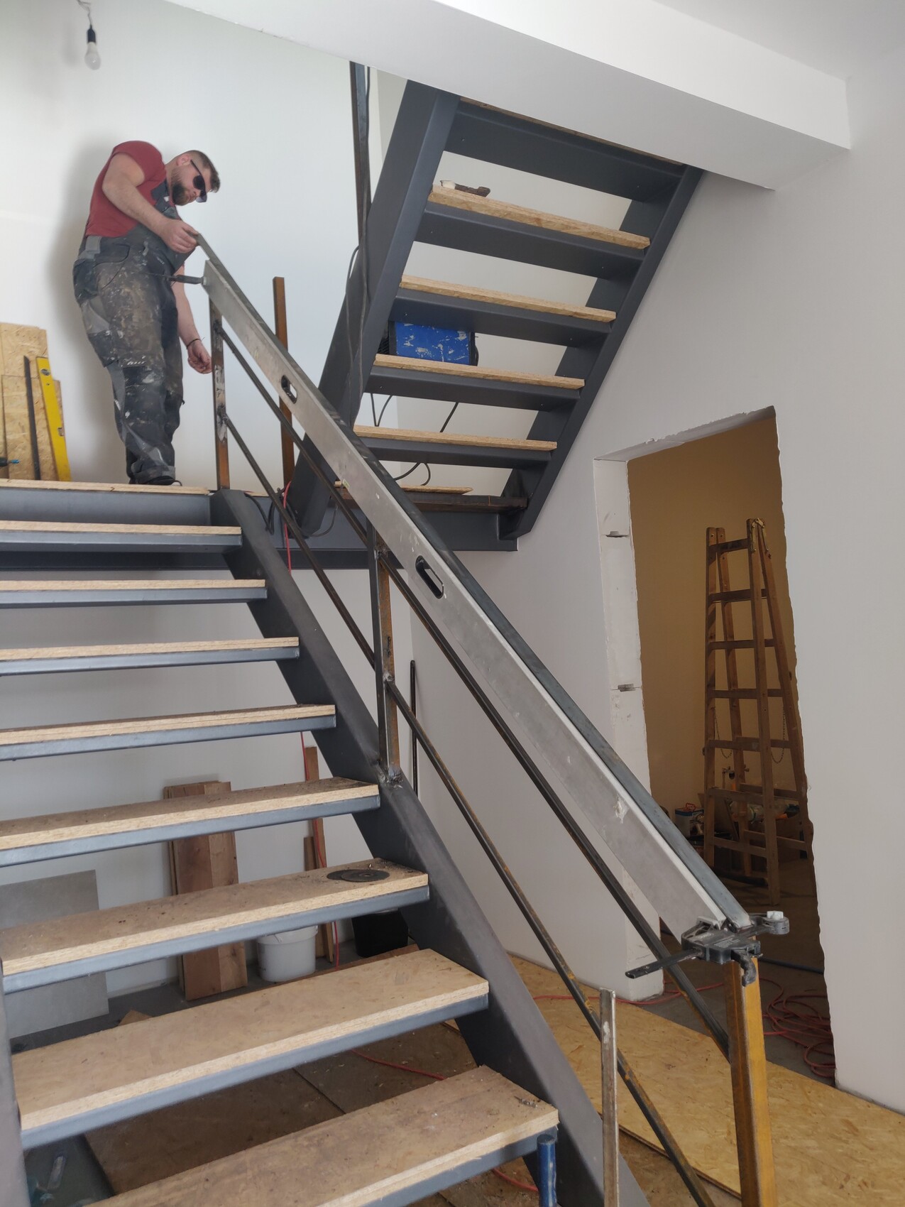 Bauarbeiter auf einer Metalltreppe arbeitet am Geländer in einer Innenbaustelle.