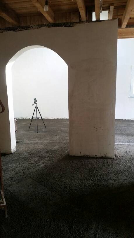 Innenraum einer Baustelle mit Bogenöffnung, Betonboden, weißen Wänden und Stativkamera
