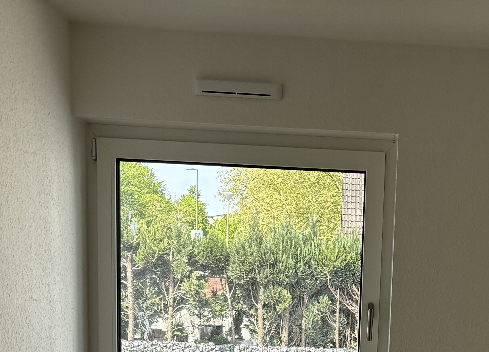 Innenraumfenster mit Lüftung darüber; Blick auf Bäume, Laterne und Dachziegel.