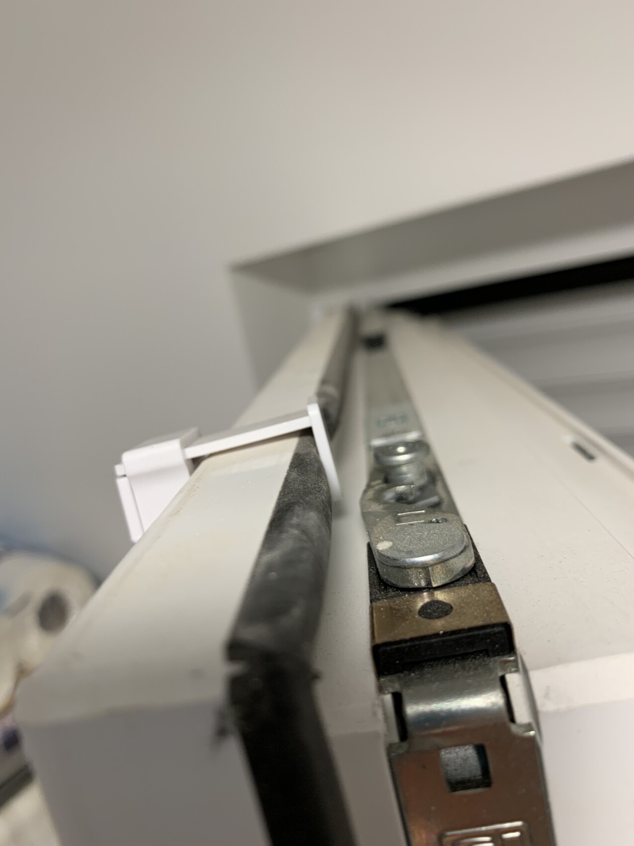 Nahaufnahme eines Fenster-Scharnier- und Hebelbereichs mit Metallteilen und Gummi-Dichtung.