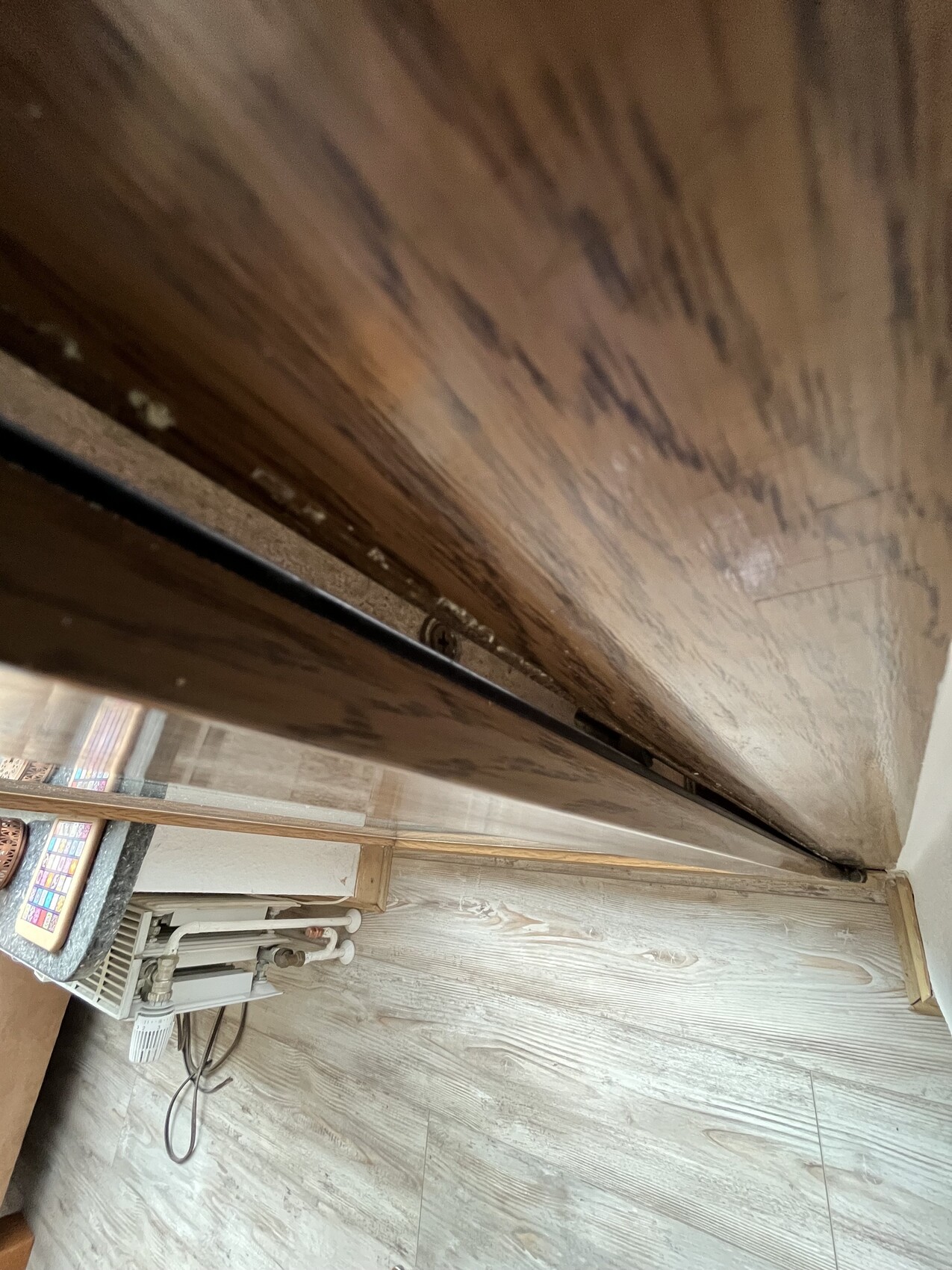 Innenraum mit Holzboden, Heizkörper und sichtbaren Rohren nahe Türrahmen.