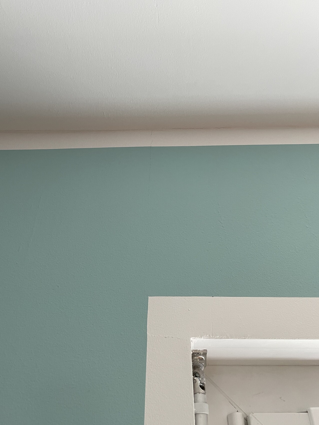Tealfarbene Wand, weiße Decke; offener Türrahmen mit sichtbaren Rohren dahinter.