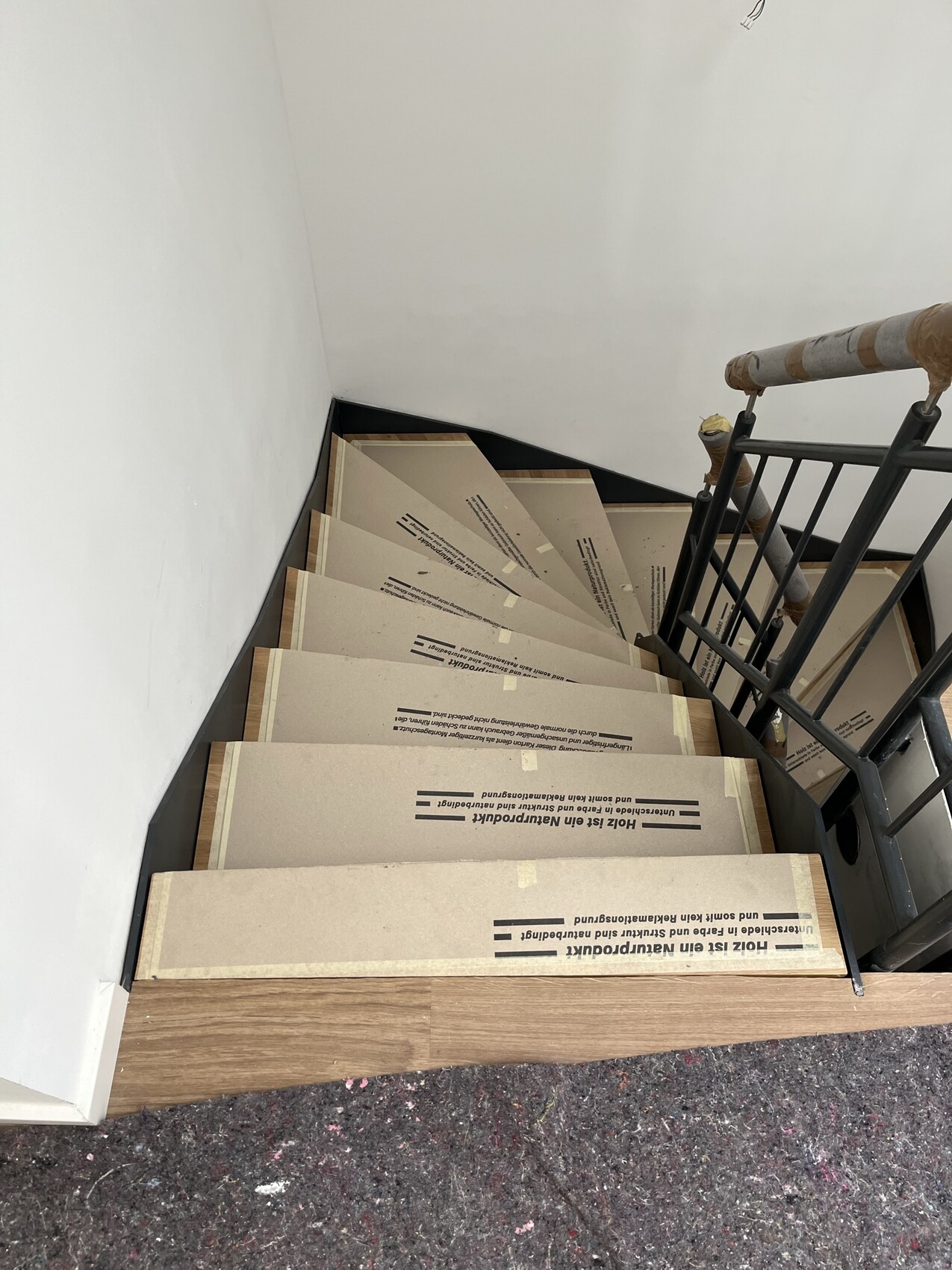 Stufen einer engen Treppe mit Kartonschutz auf jeder Stufe, rechts Metallgeländer, Baustellenzustand.