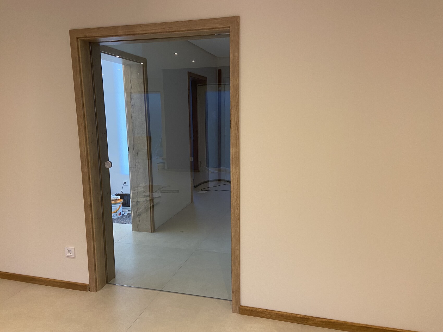 Offene Holztür mit Glasrahmen führt in einen hellen Flur; links Bauutensilien sichtbar.
