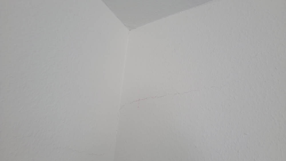 Weiße verputzte Wand-Ecke mit leichter Struktur und feiner Risslinie