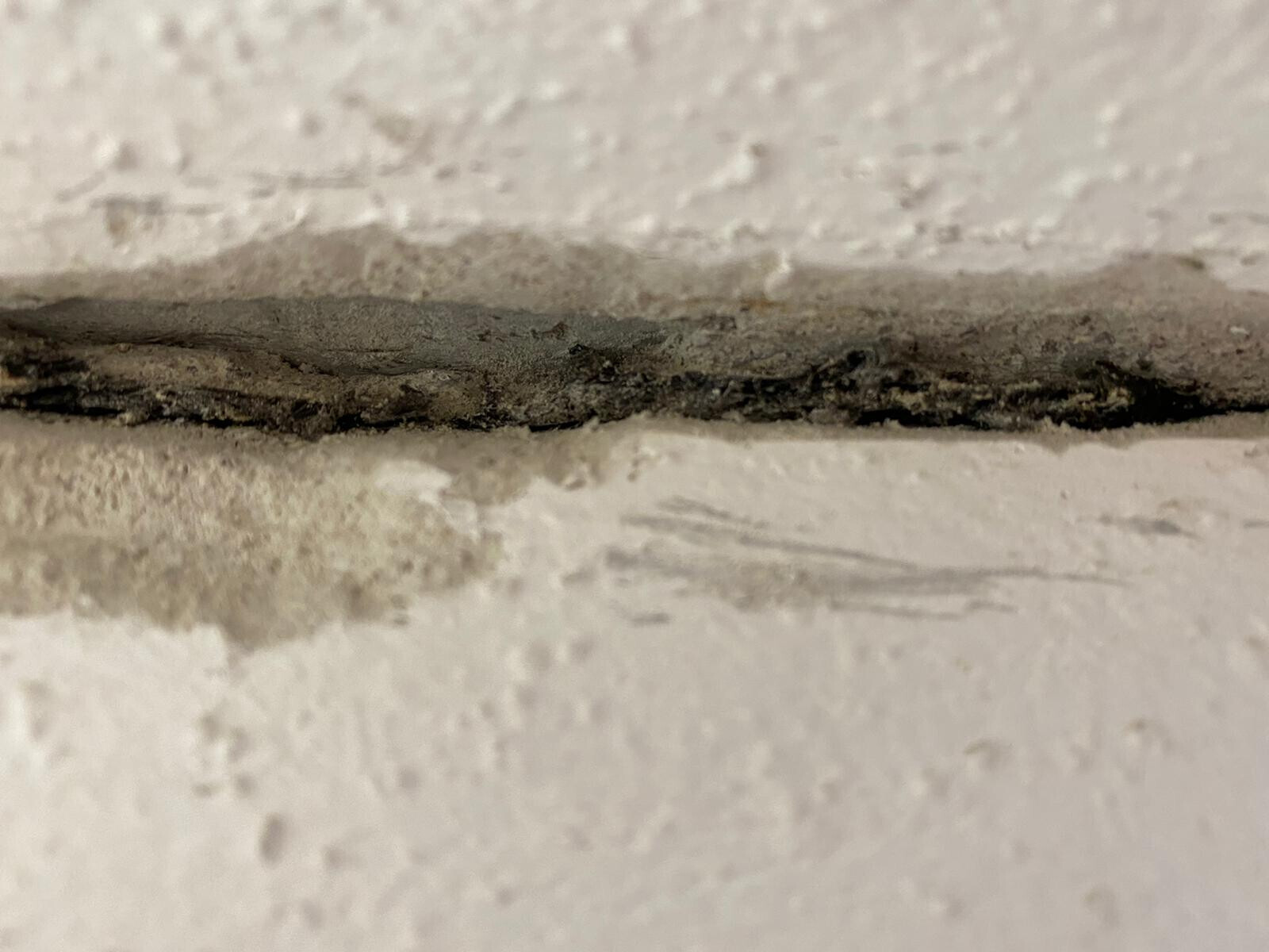 Dunkler Spalt in einer rauen weißen Wand mit Staub und Schmutz.