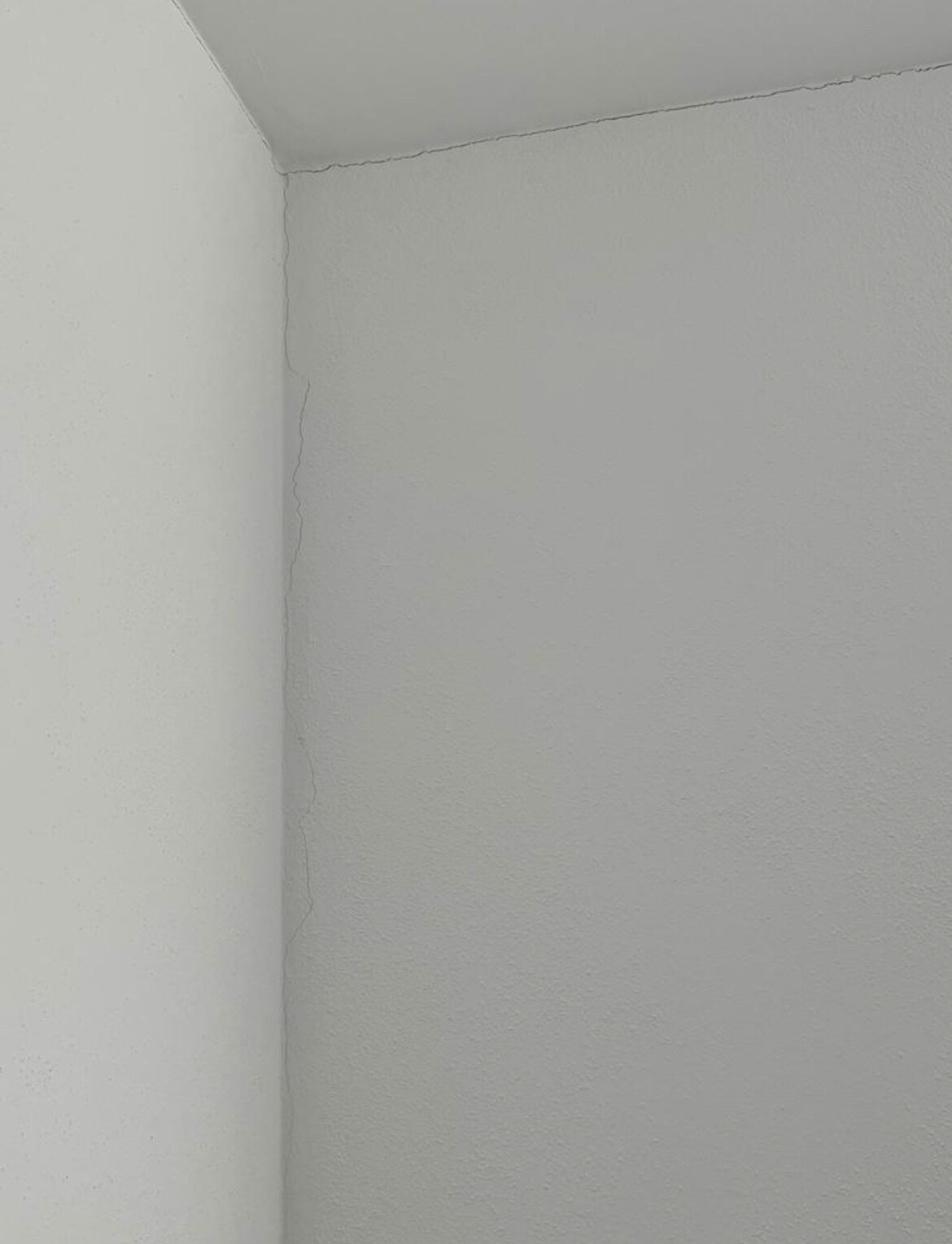 Winkel eines hellgrauen Zimmers mit feinem Riss entlang der Wand- und Deckenfuge