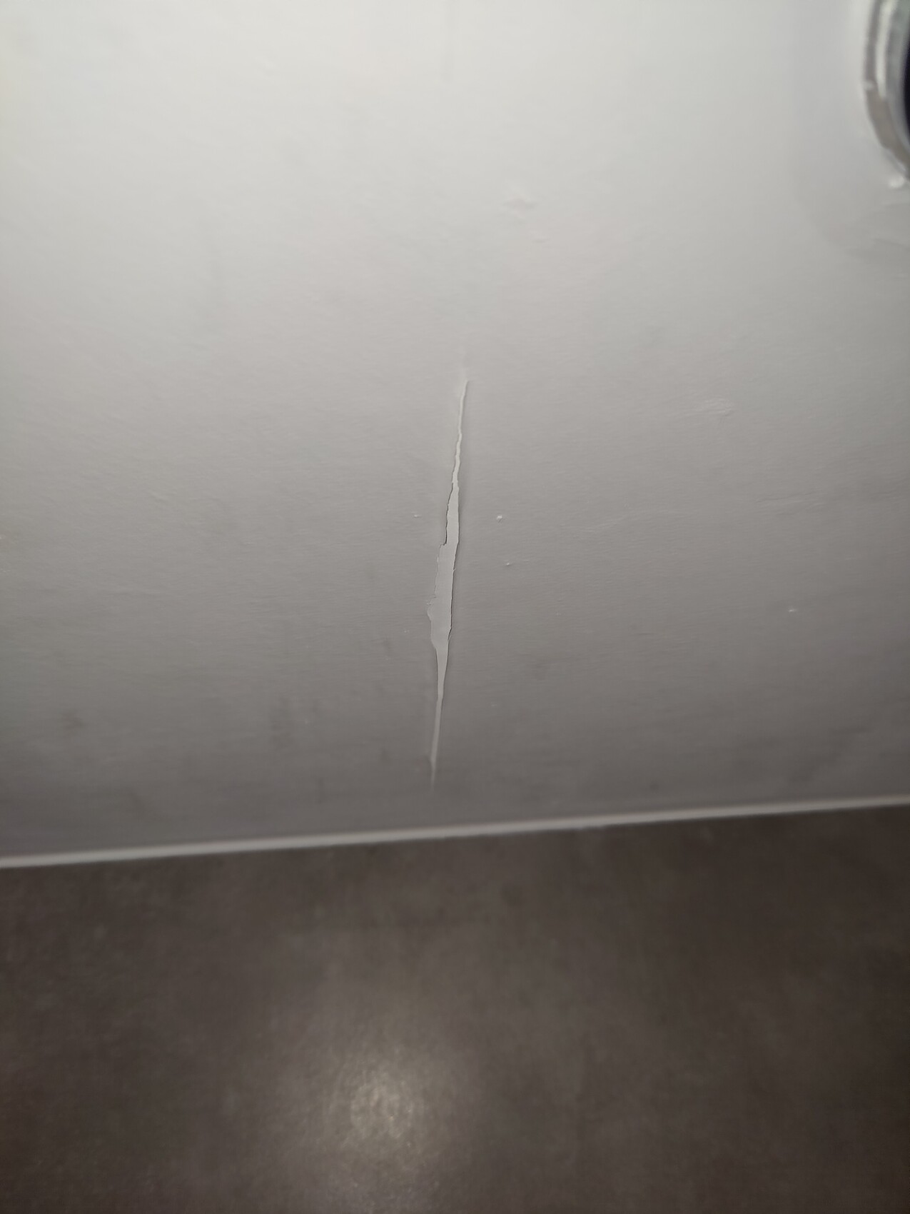 Helle Wand mit senkrechtem Riss von oben nach unten, dunkler Boden darunter.