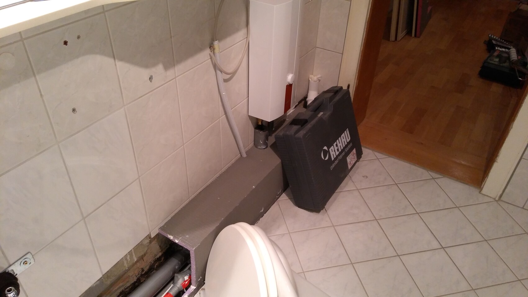 Badezimmer: offene Installationen am Boden, Rohre, Heizgerät, REHAU-Werkzeugkoffer neben Toilette.