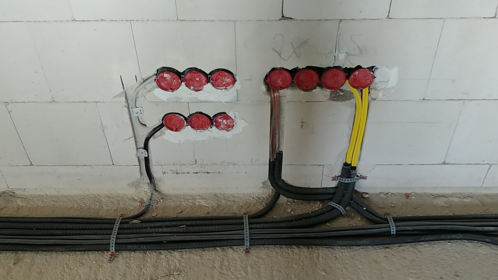 Verlegte Kabel in Wand mit roten Abdeckkappen und Kabelkanälen auf der Baustelle