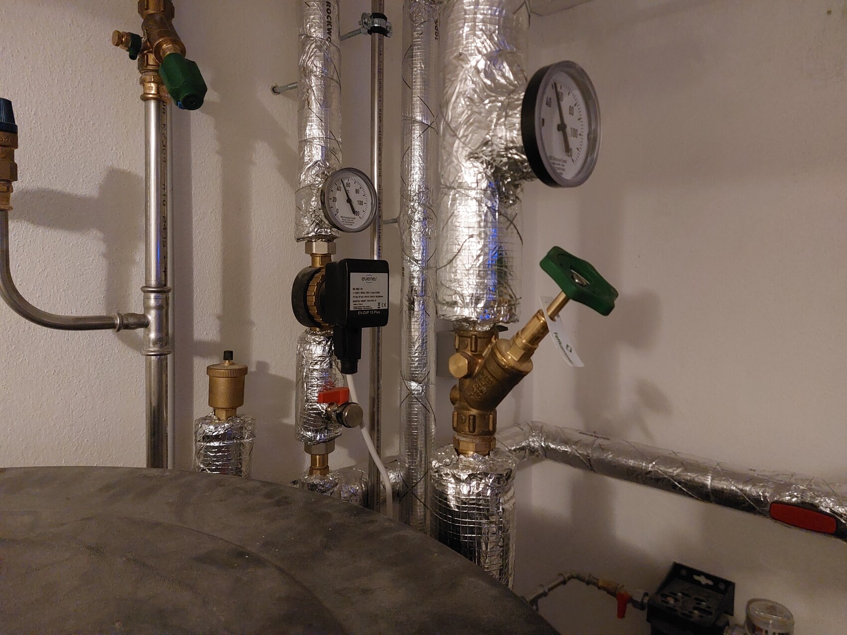 Installierte Heizungsrohre, Messgeräte, Ventile und Isolierung in einem Technikraum.