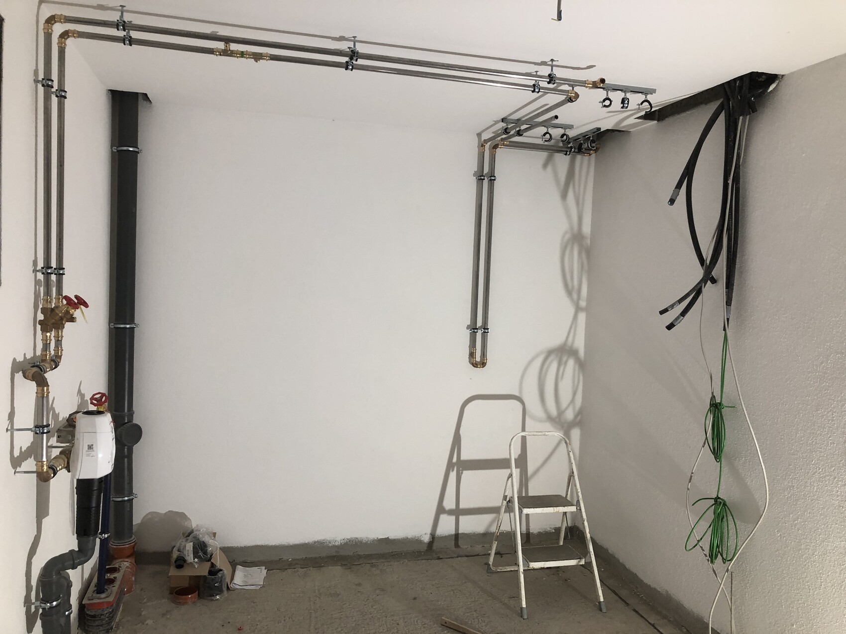 Technikraum mit Rohren, Ventilen, Pumpe, Leiter und Schläuchen an der Wand.