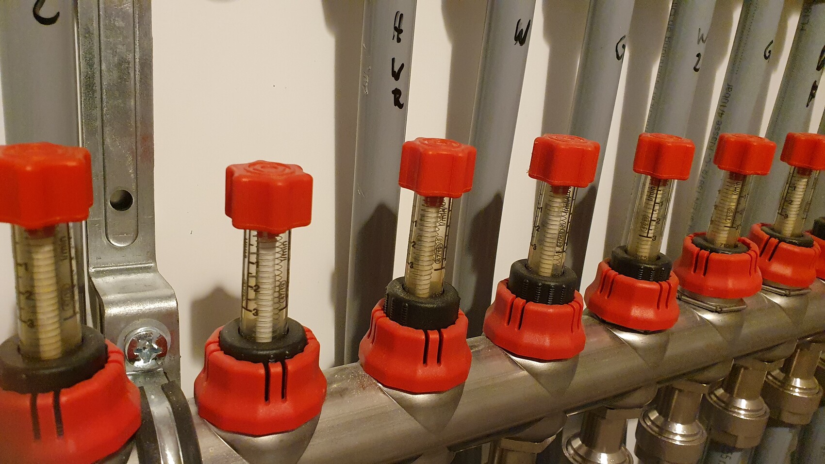 Mehrere rote Griffventile mit Skalen an einer Edelstahl-Verteilungsleiste in einer Industrieanlage.