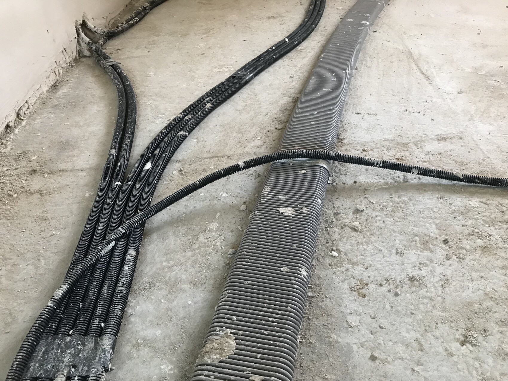 Baustelle mit schwarzen Kabelsträngen auf dem Rohbauboden, Kabelkanäle verlaufend.