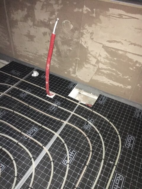 Unterboden-Heizrohre in Schlaufen auf Dämmplatte, rotes Kabel ragt aufrecht hervor.