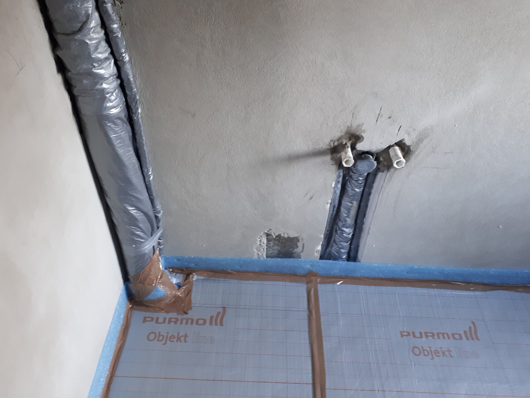 Isolierte Heizungsrohre an der Decke, Rohre mit Dämmung und blauer Folie.