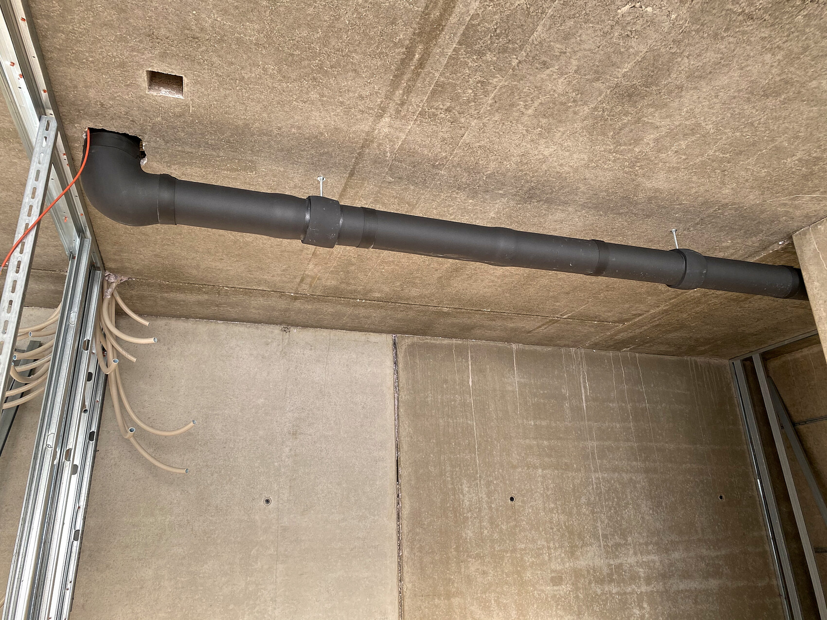 Schwarzes Rohr an der Decke mit Biegung, befestigt mit Clips; daneben Kabelbündel.