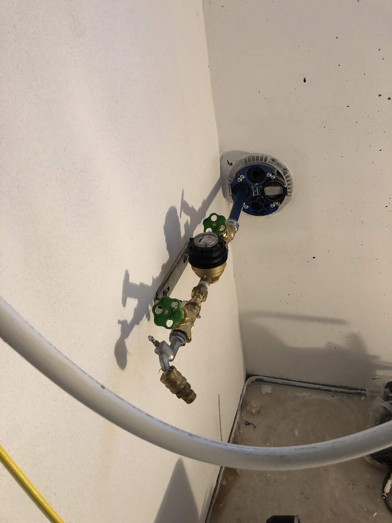 Wasseranschluss an der Wand mit Zähler, grünen Absperrventilen und Schlauch.