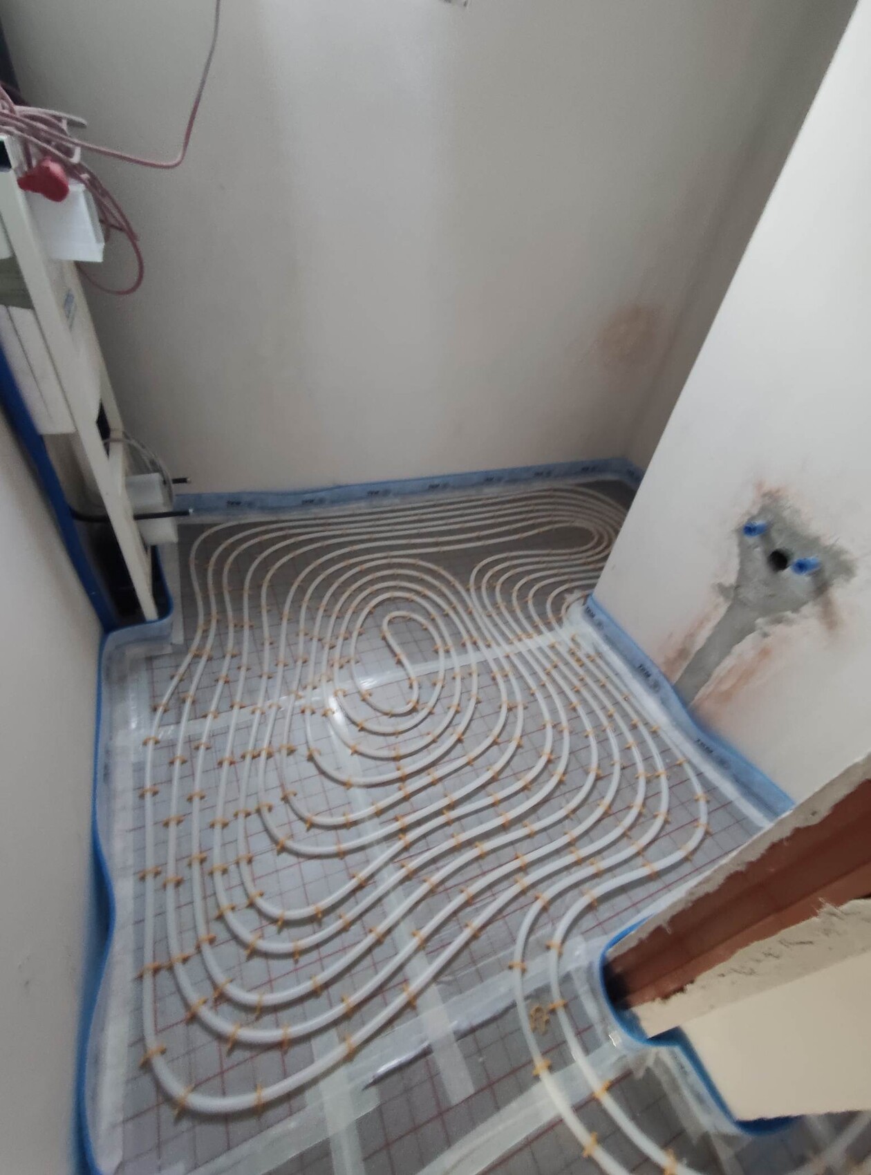Raum mit Fußbodenheizung: weiße Rohre spiralförmig auf Dämmunterlage, Installationsbereich.