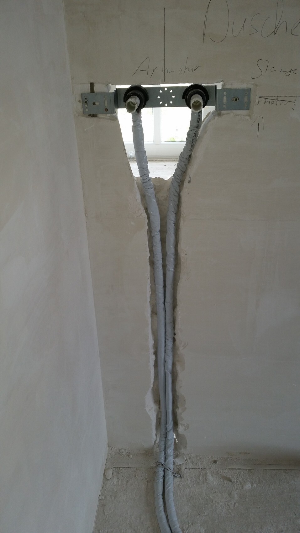 Zwei isolierte Wasserleitungen verlaufen senkrecht durch eine Wand.