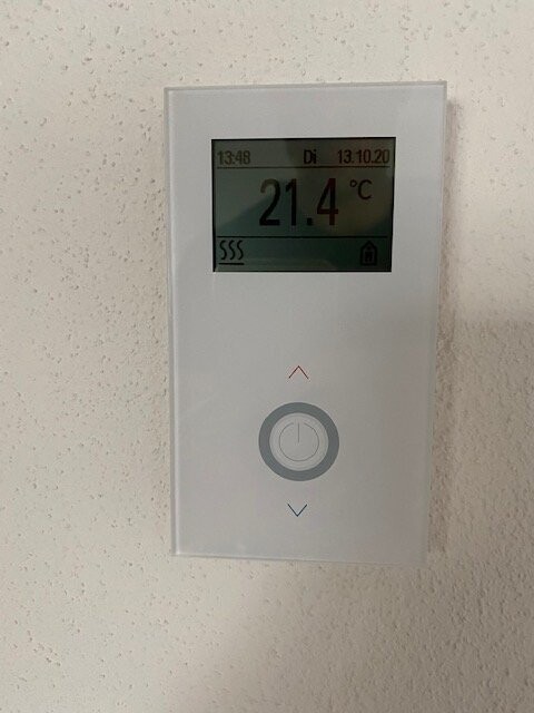 Wandthermostat mit Display: 21.4 °C, Datum/Uhrzeit, Up/Down-Pfeile, runder Knopf.