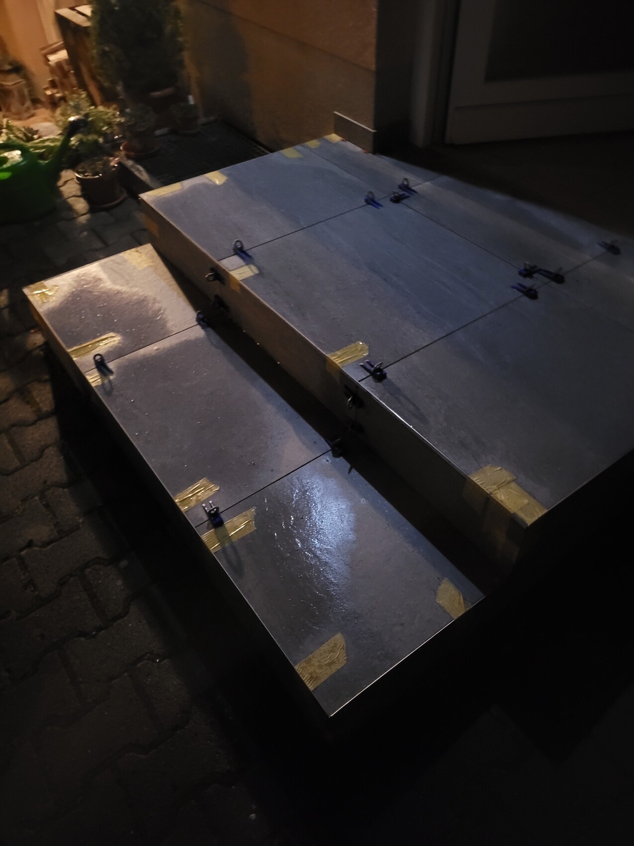 Zwei große Metallplatten mit Klebeband und Clips liegen auf einem Pflasterweg beim Nachtlicht.