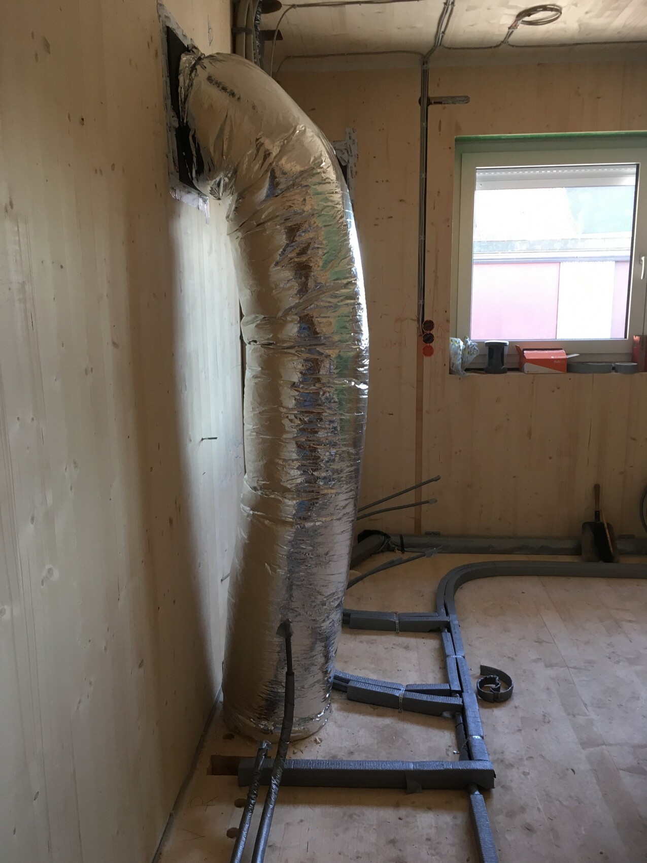 Rohbauzimmer mit isolierter Luftleitung, Rohren und Fenster während der Bauarbeiten.