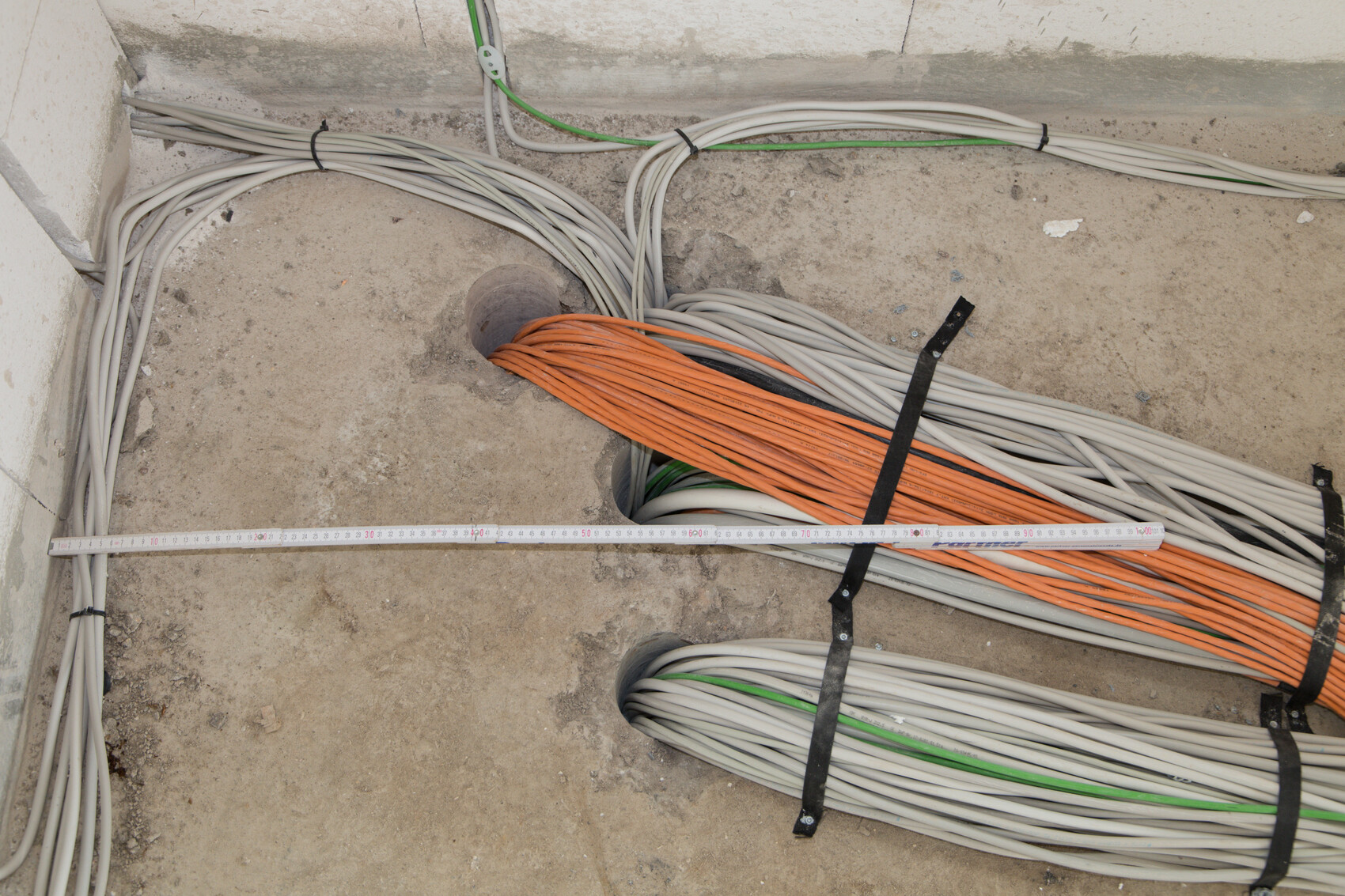 Baustelle mit orange und grauen Kabelbündeln auf Boden, Messband sichtbar