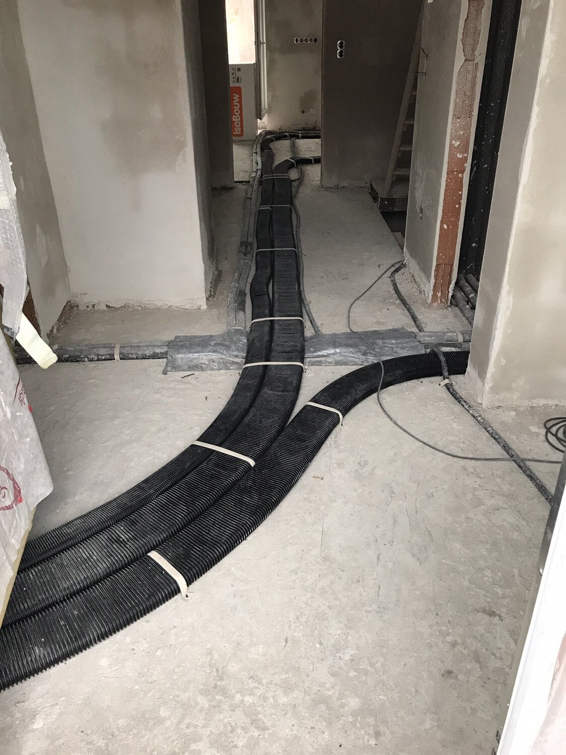 Baustelle: Schwarze Kabelkanäle verlaufen auf dem unfertigen Boden durch einen Gang.