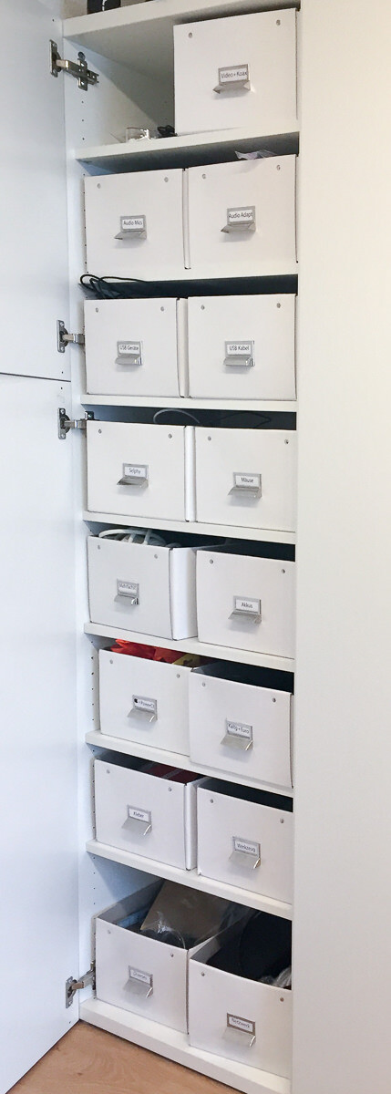 Hohe weiße Schrankreihe mit beschrifteten Boxen zur Kabel- und Technikorganisation.