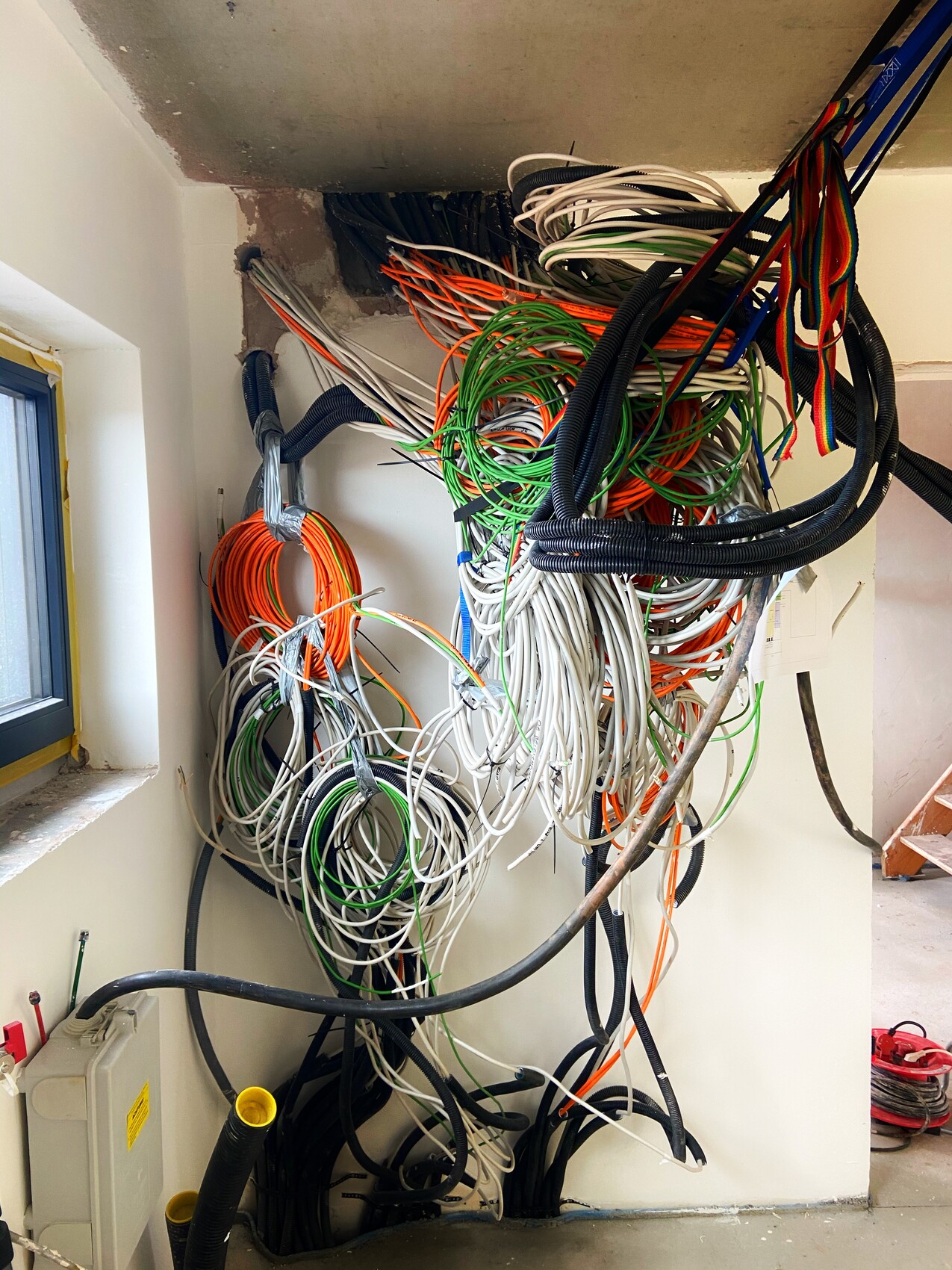 Verhedderte, bunte Kabelbündel in einem Installationsraum hinter einer Wand.