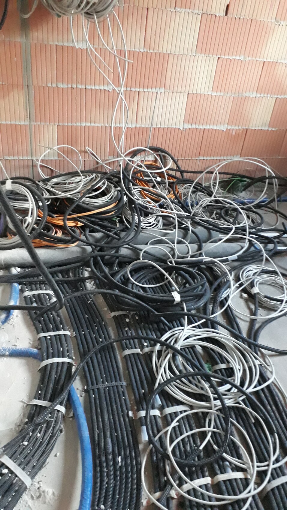 Chaotische Kabelbündel und lose Leitungen vor einer Backsteinwand auf einer Baustelle.