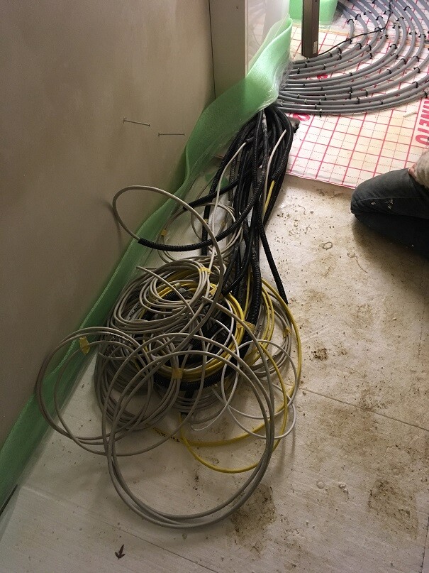 Verhedderte Kabelstränge auf dem Bauboden neben einer Wand.