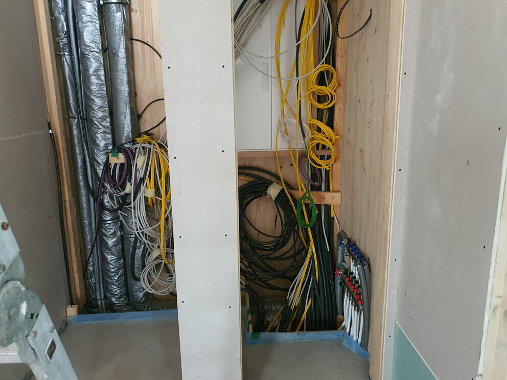 Kabelsalat in einer Bauwand: gelbe, grüne und schwarze Leitungen rund um Holzrahmen