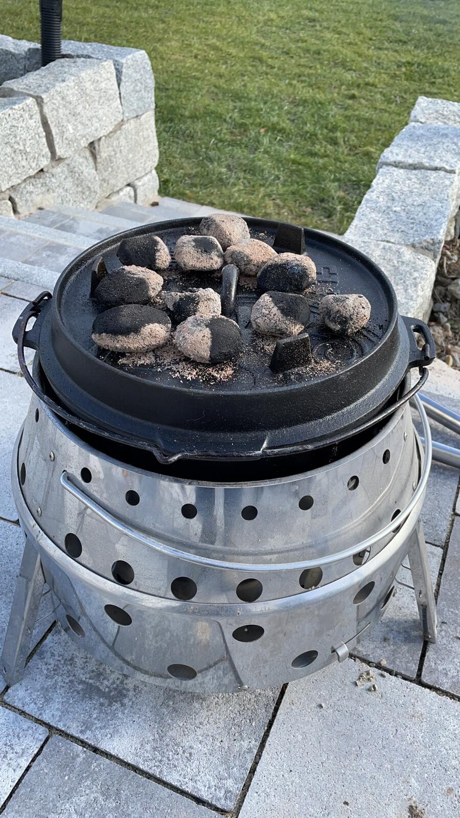 Runder Kamado-Grill mit Kohlebriketts auf dem Deckel, im Garten.